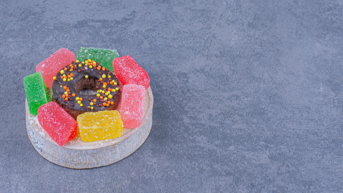 Разноцветные мармеладные конфеты и пончик на сером столе