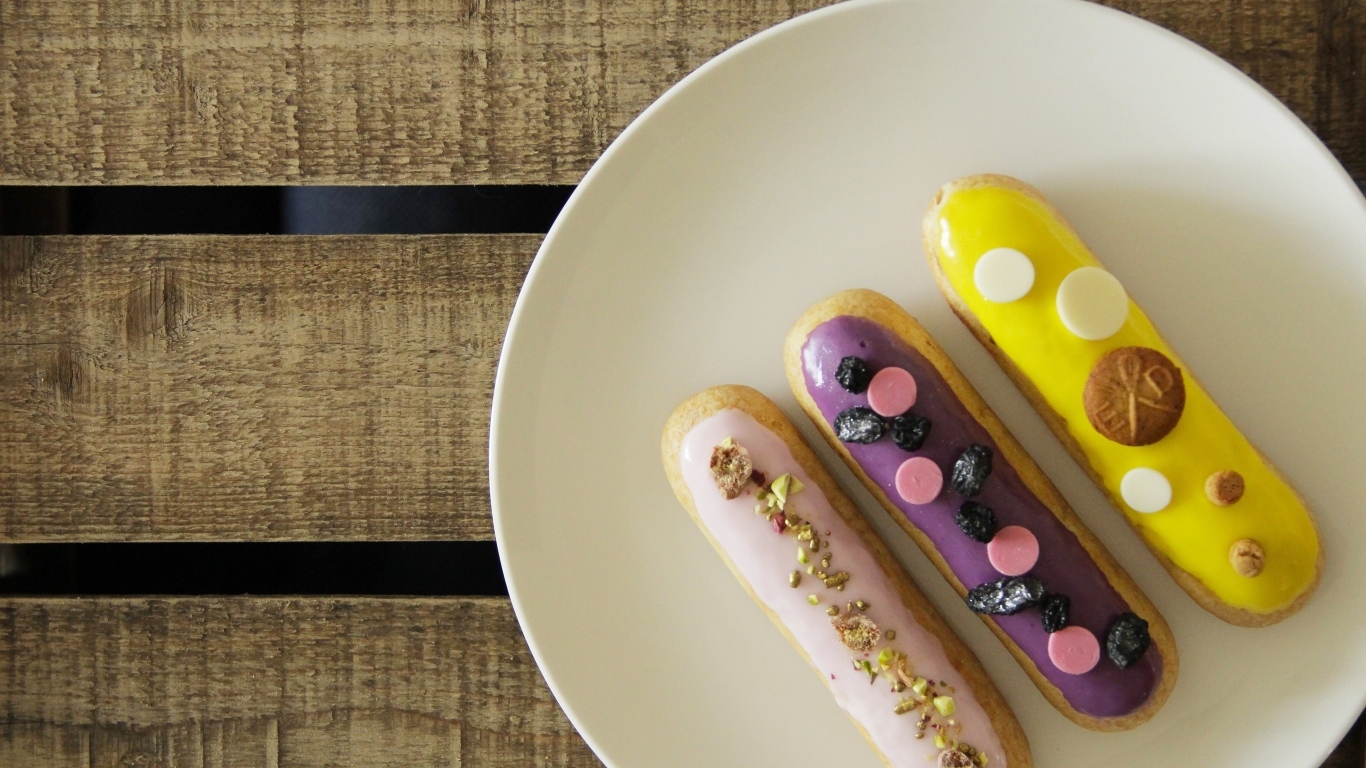 Три эклера на белой тарелке на деревянном столе