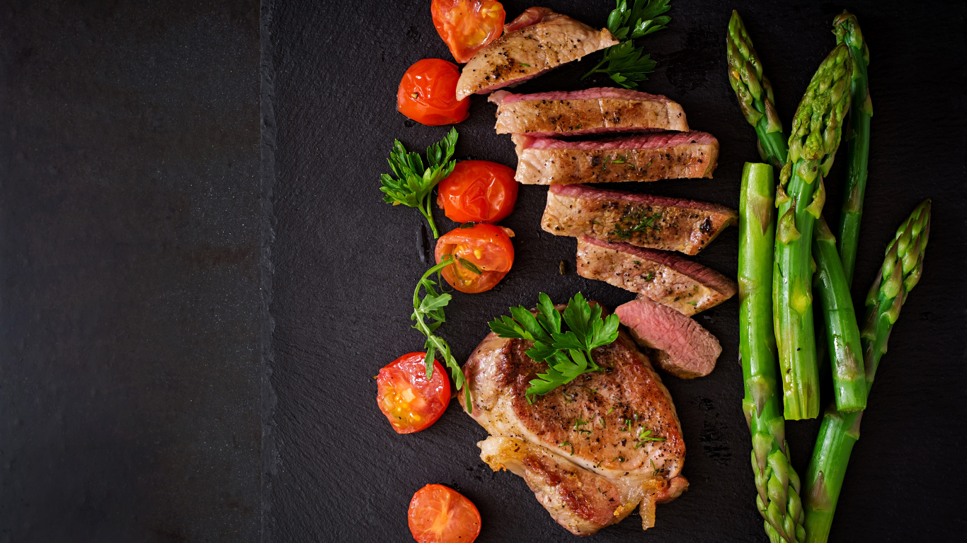 Нарезанный кусок мяса с помидорами и зеленой спаржей