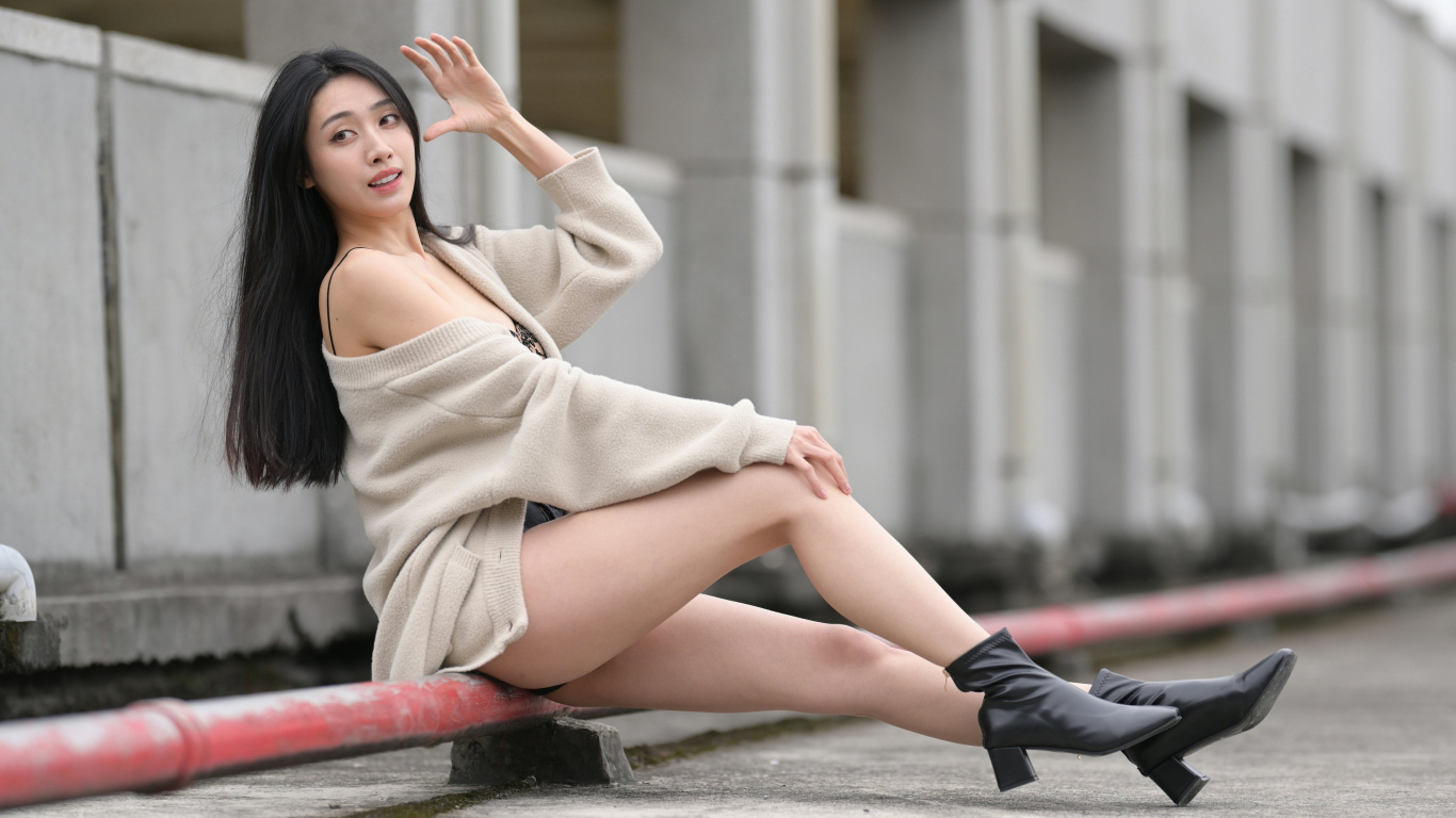 Девушка азиатка в теплой кофте сидит на трубе