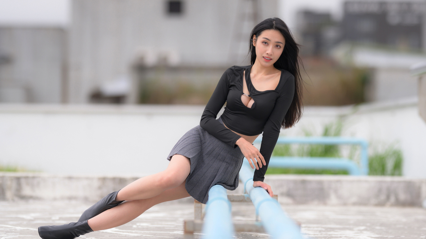 Девушка азиатка в черном наряде сидит на трубе