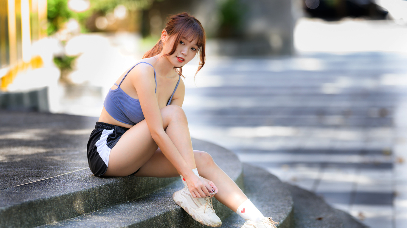 Азиатка в шортах сидит на ступеньках