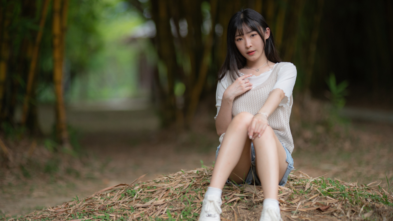 Азиатка сидит на земле в парке