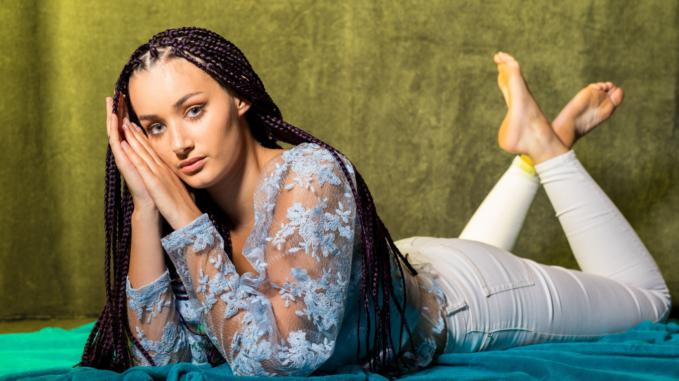 Брюнетка с косами на голове лежит на постели