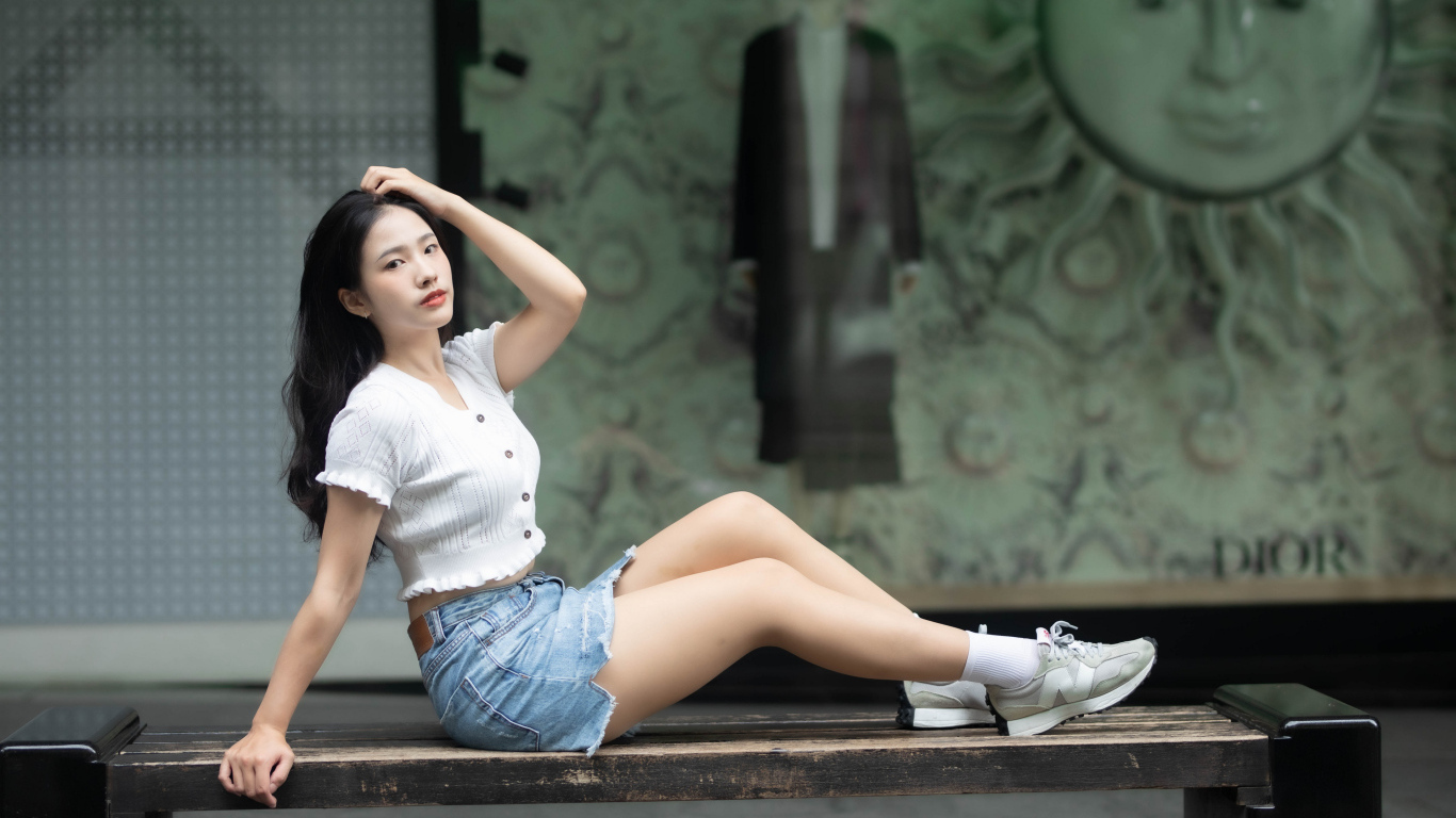 Милая девушка азиатка в белой кофте лежит на лавке