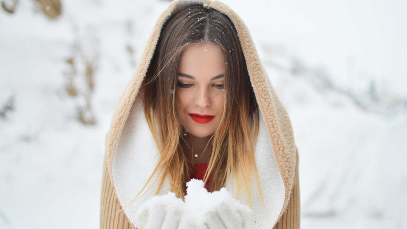 Милая девушка в капюшоне держит снег в ладонях