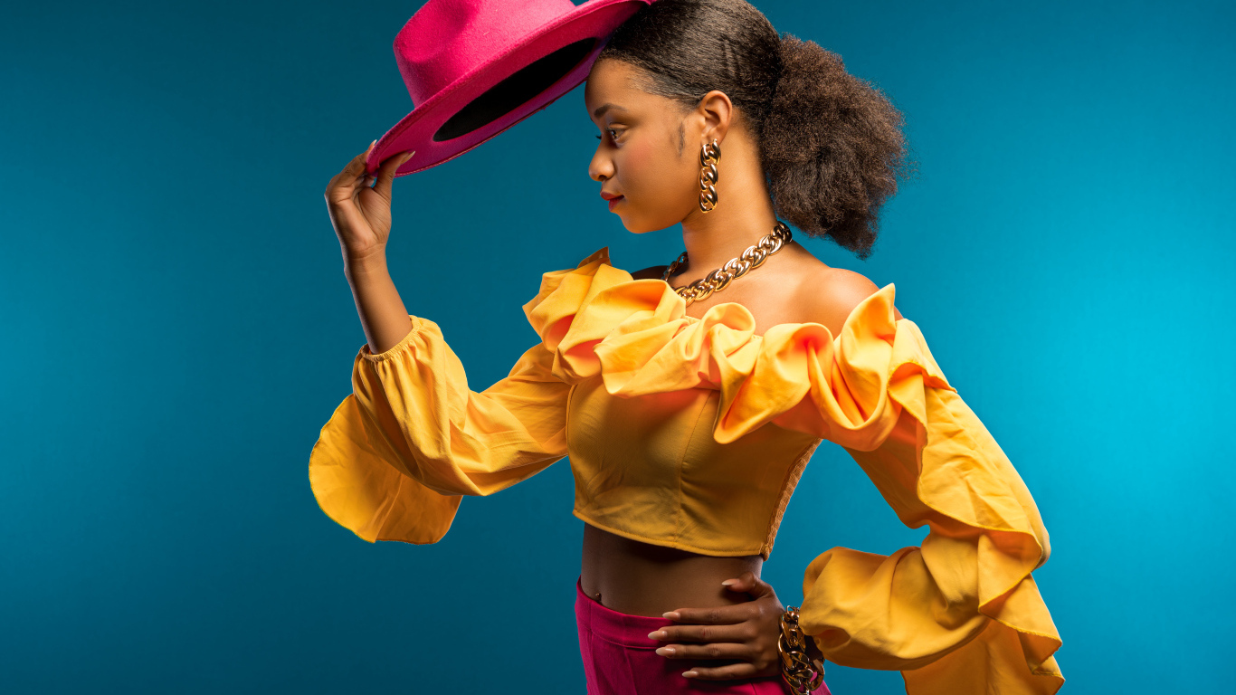 Темнокожая девушка в костюме с красной шляпой в руке