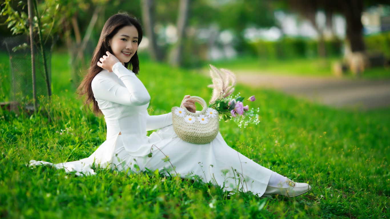 Нежная азиатка в белом наряде сидит на траве