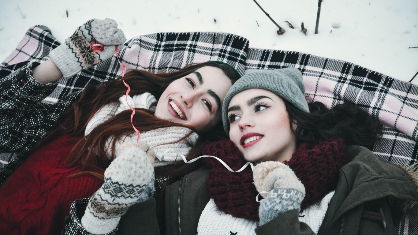 Две красивые молодые девушки лежат на снегу