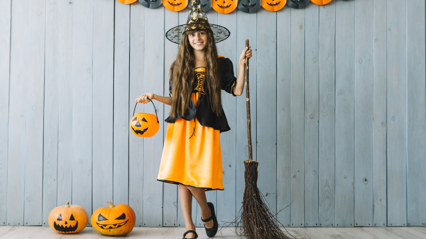 Девочка в костюме ведьмы у стены с декором на Хэллоуин