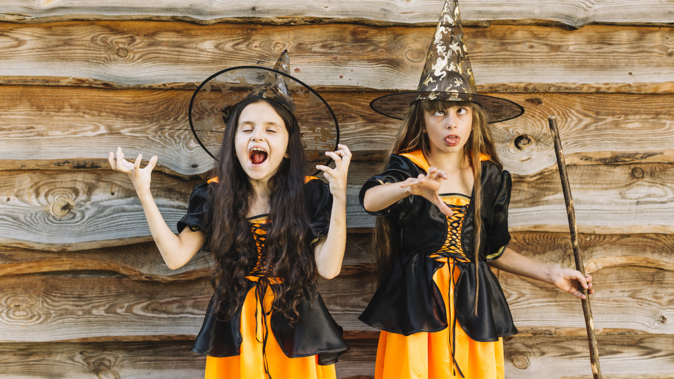 Две девочки в костюме ведьмы у стены на Хэллоуин