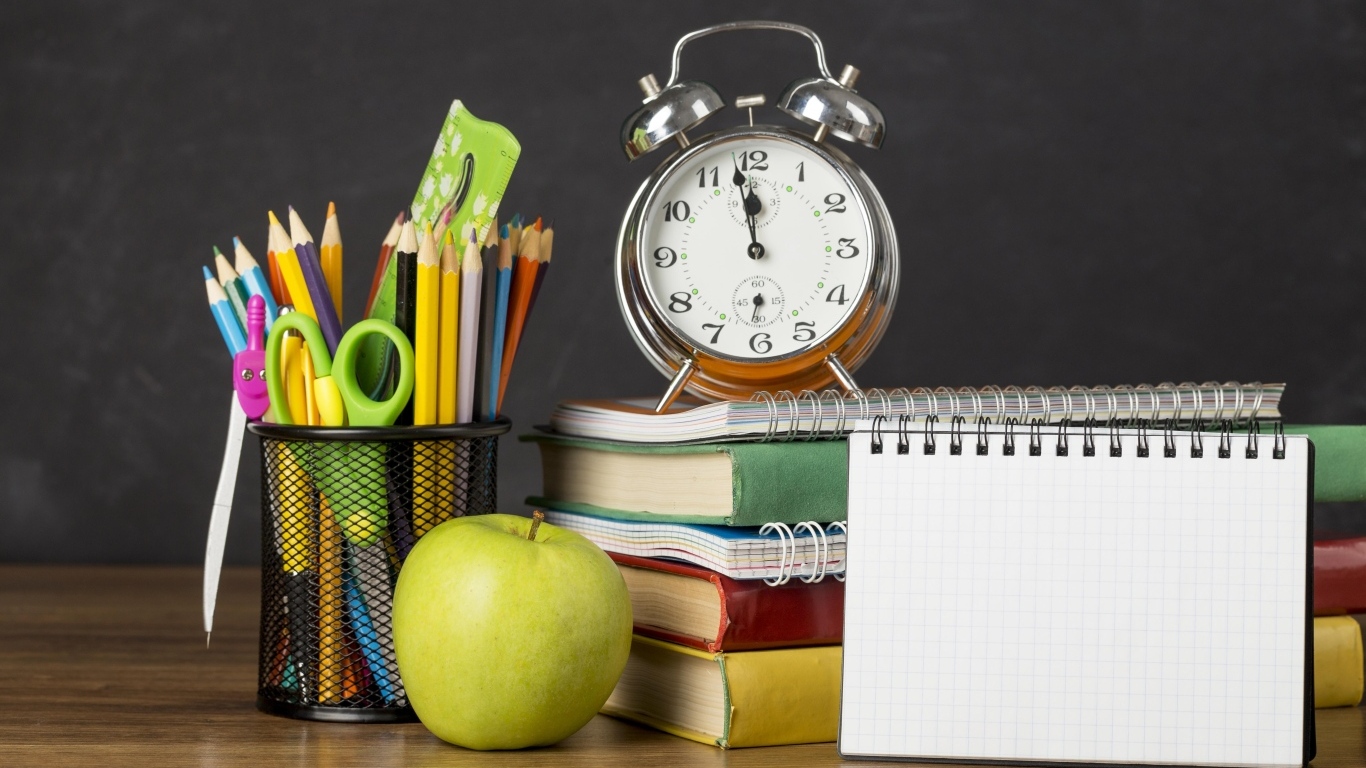 Канцелярские предметы на столе с будильником и книгами 