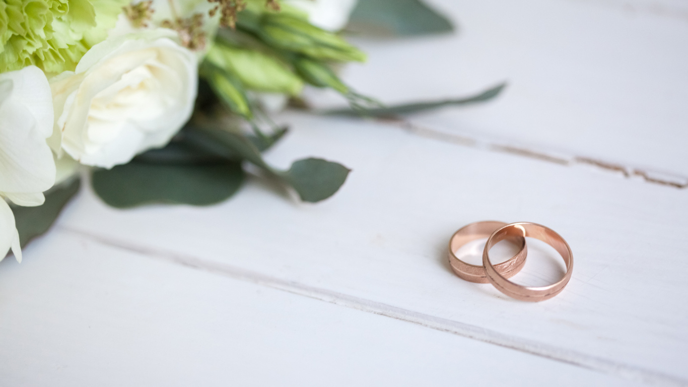 Два золотых обручальных кольца с букетом на белом столе