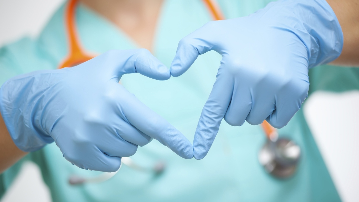 Доктор в медицинский перчатках делает сердце руками