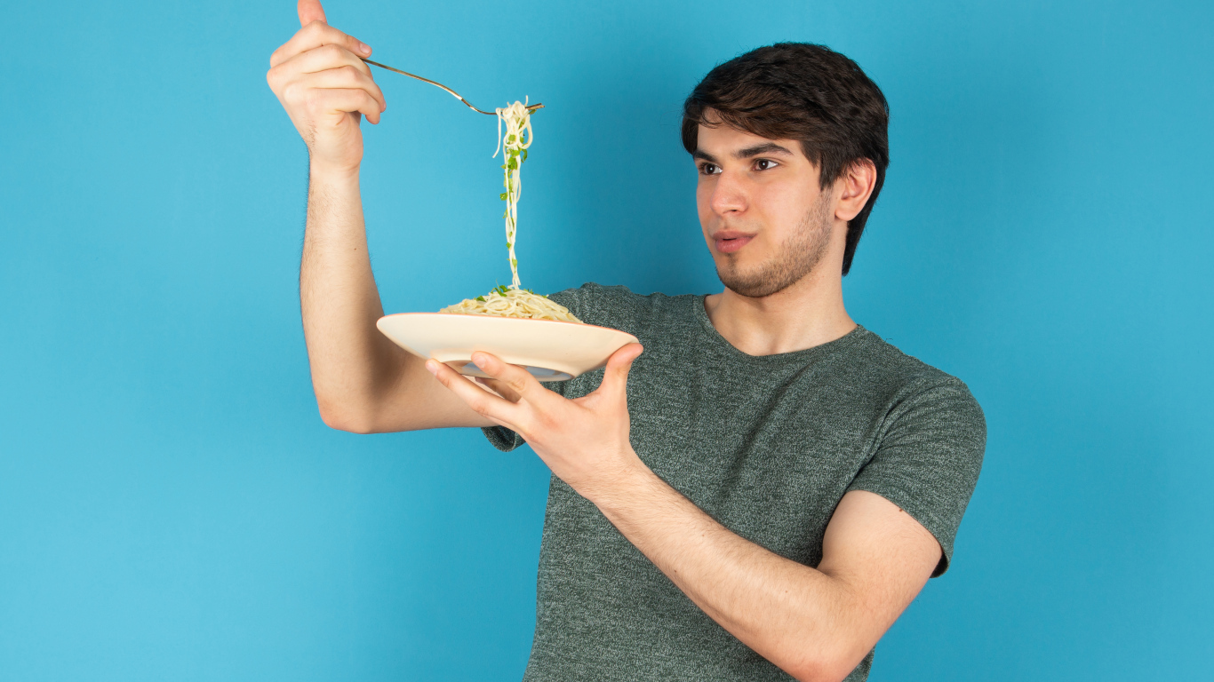 Молодой человек держит тарелку со спагетти в руках