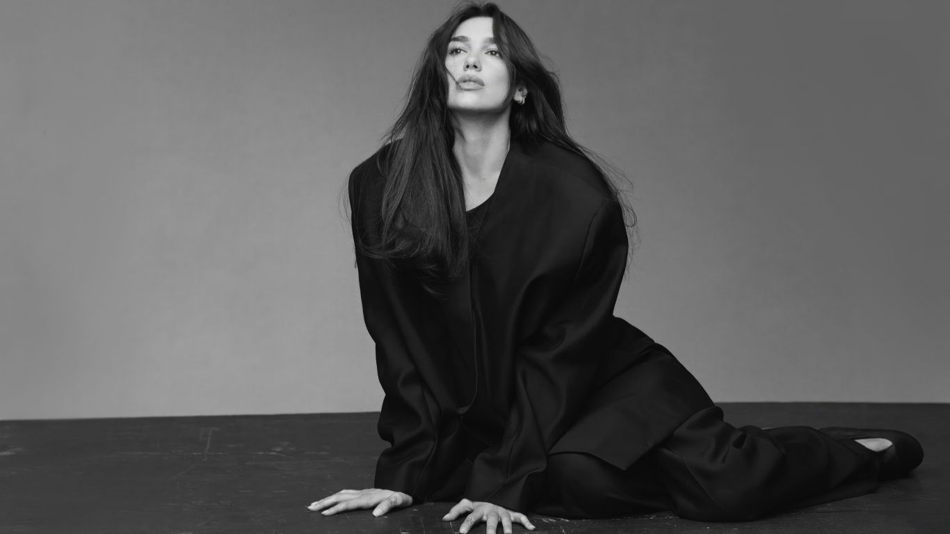 Певица Дуа Липа в черном костюме сидит на полу