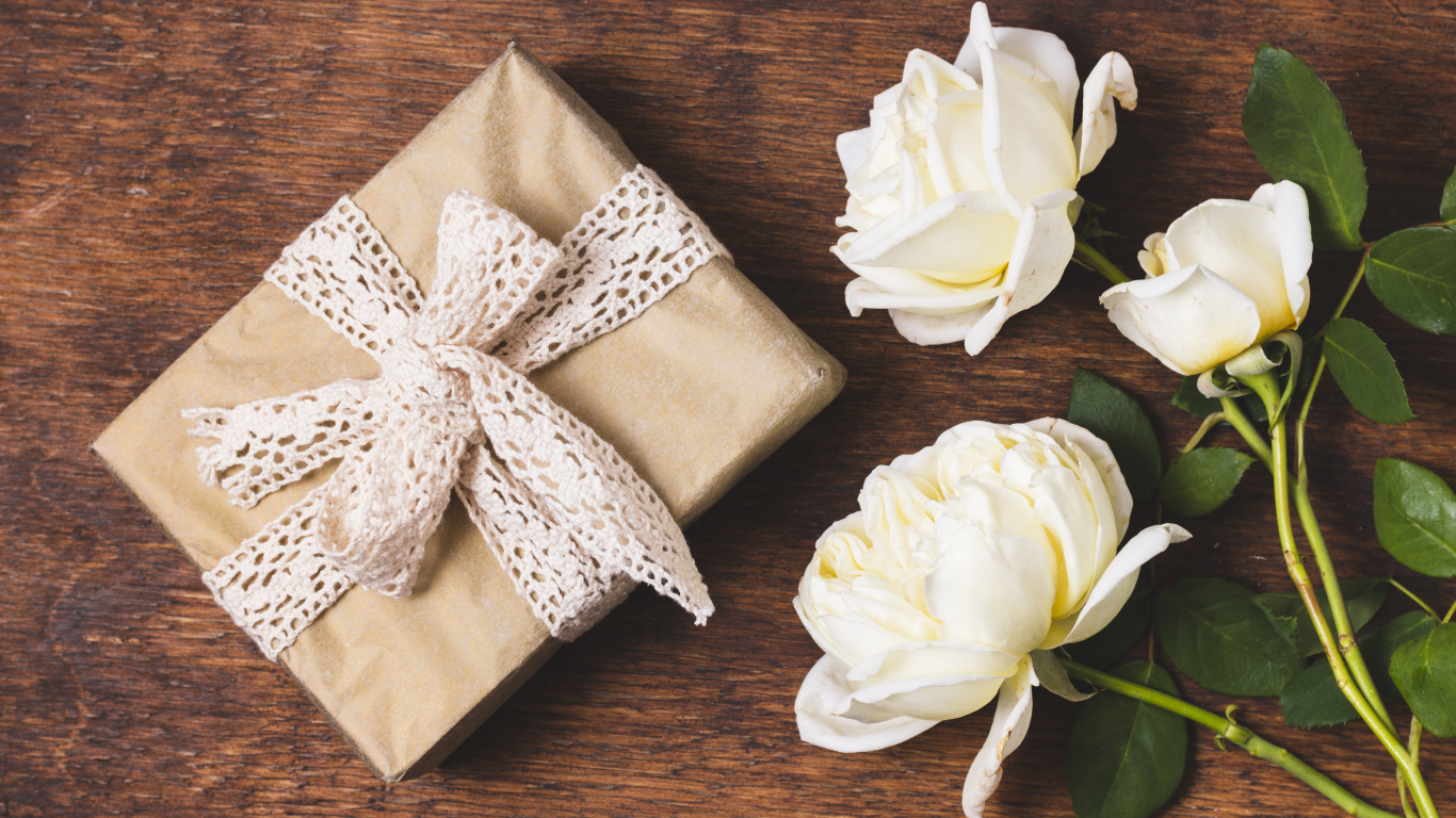 Коробка с подарком на деревянном столе с белыми розами