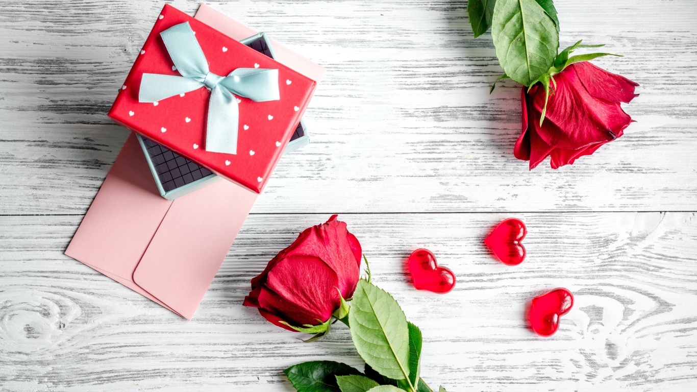 Две красные розы с подарком и сердечками на столе