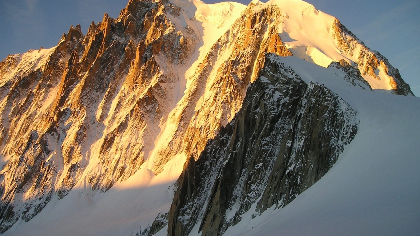 Заснеженная высокая гора в лучах яркого солнца