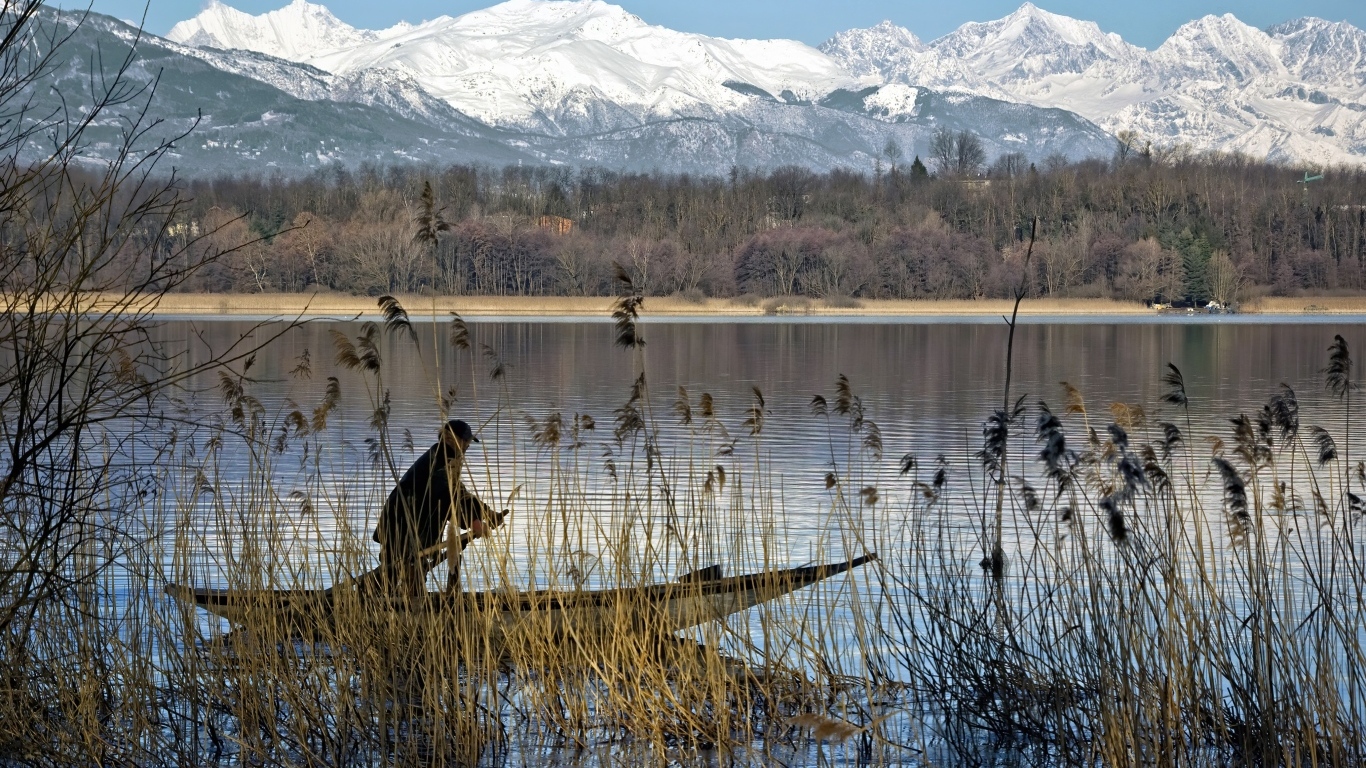 Рыбак плывет по воде на фоне заснеженных гор