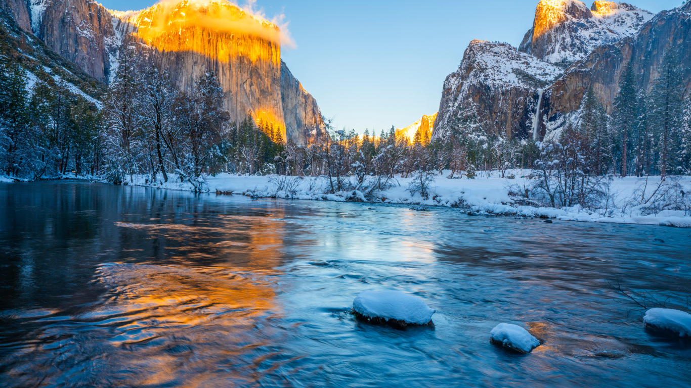 Холодная река с заснеженными берегами и горы в лучах солнца