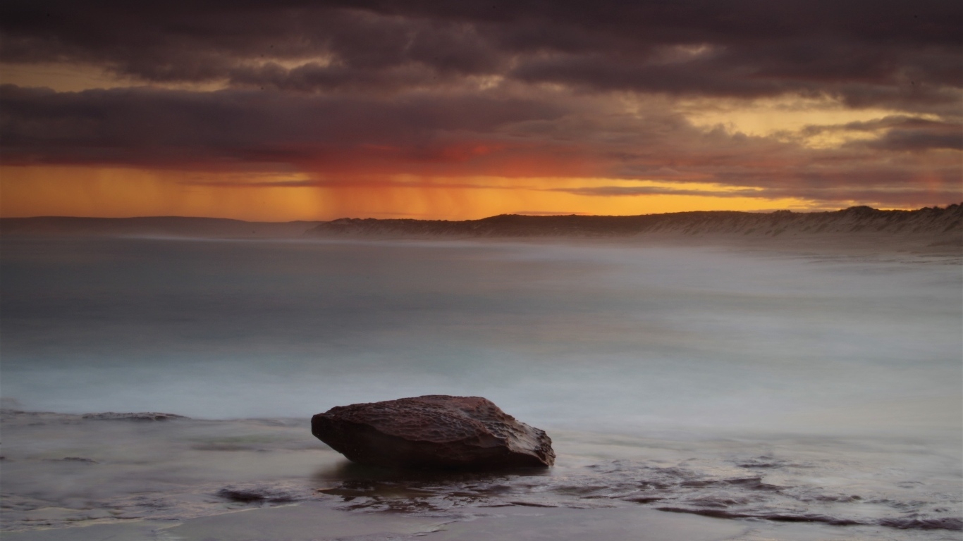 Большой камень в воде на фоне грозового неба в море