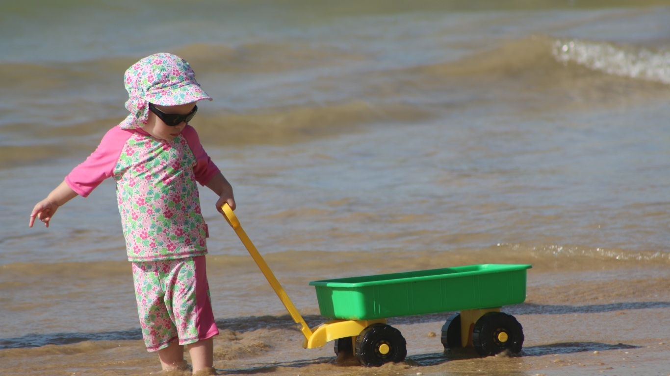 Девочка с машинкой играет на песке у моря