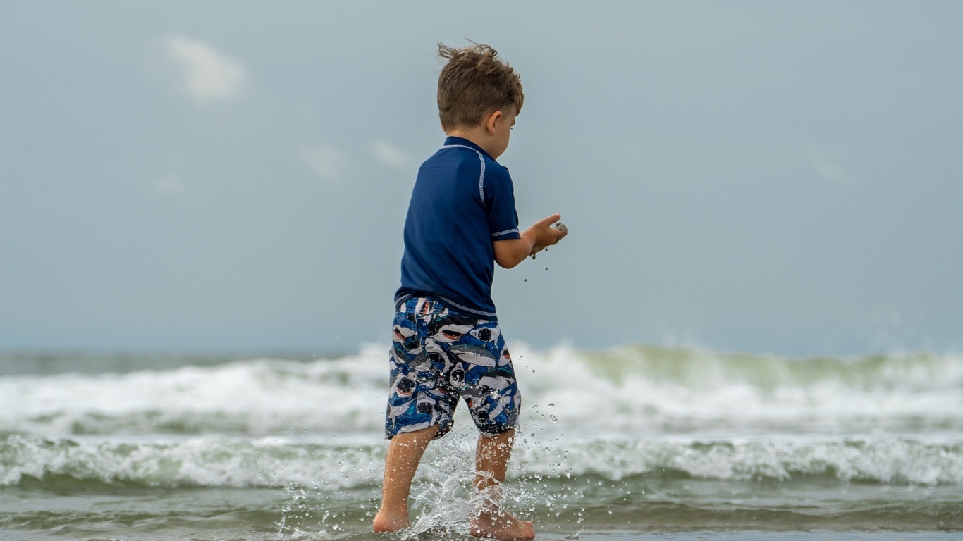 Маленький мальчик гуляет по воде у моря