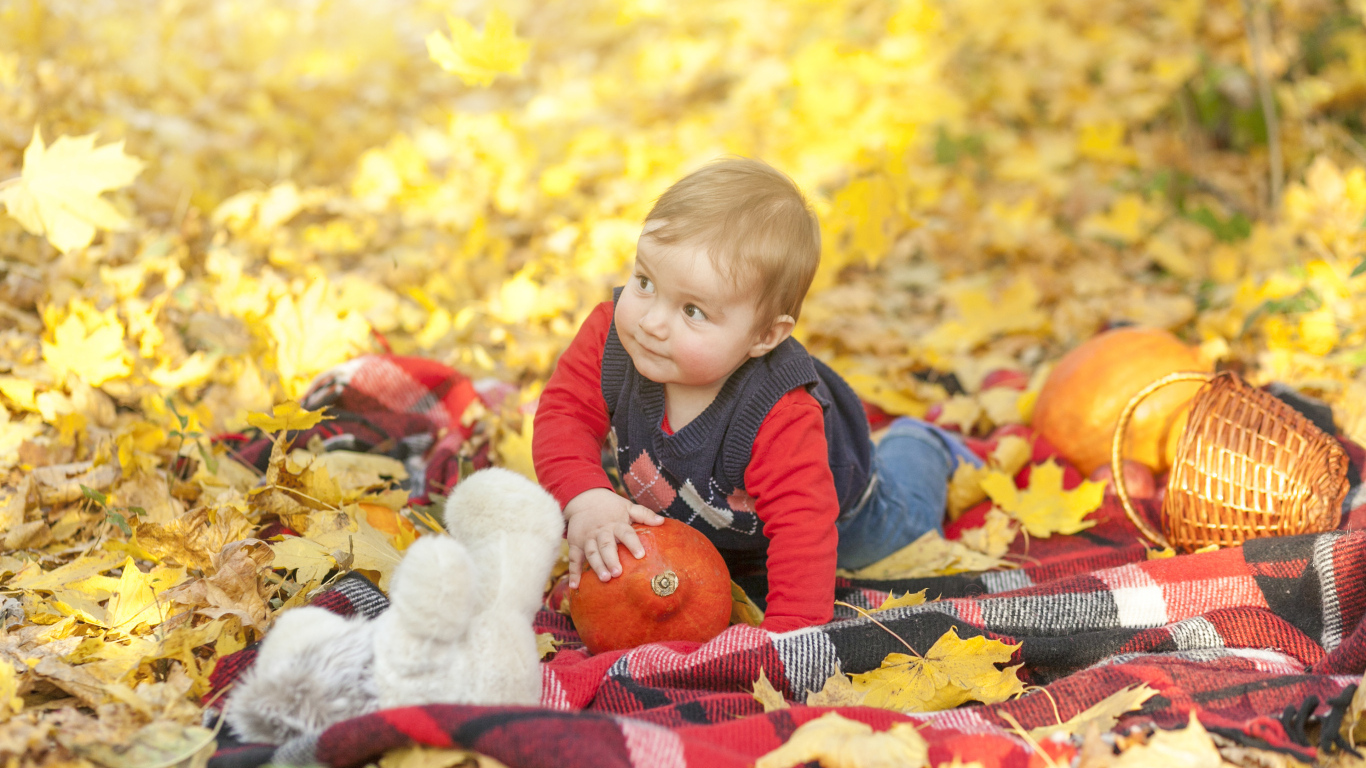 Маленький ребенок лежит на покрывале на земле осенью