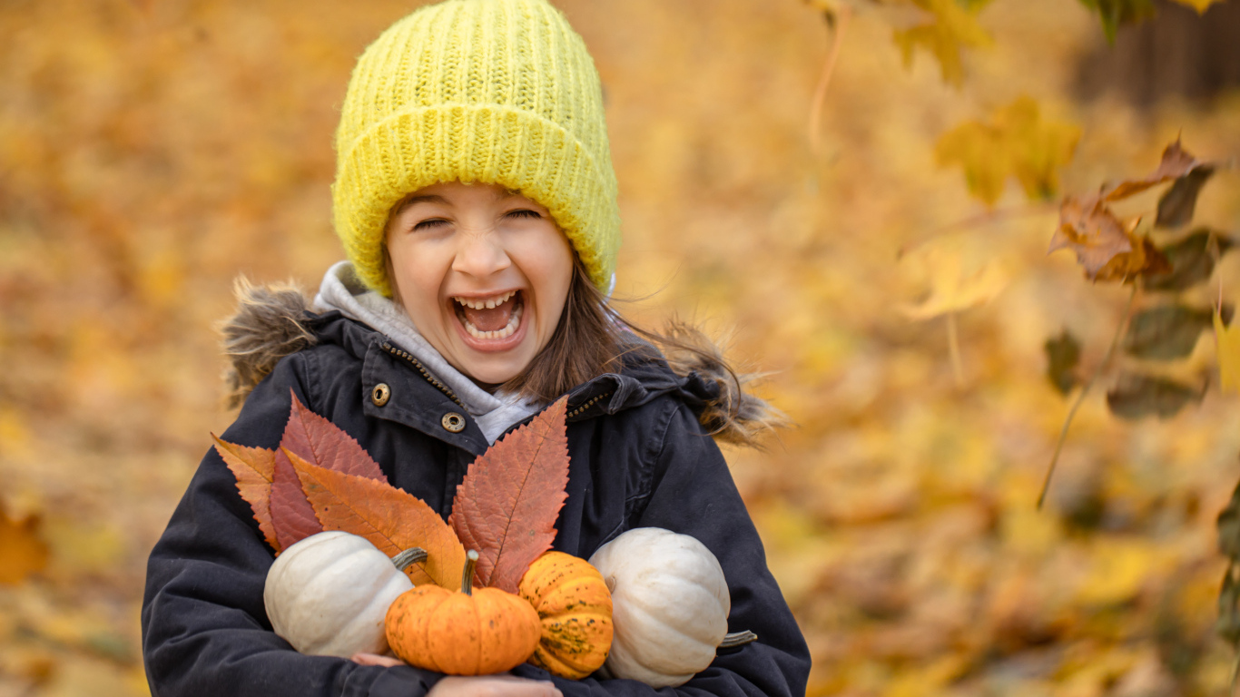 Cheerful girl with pumpkins and leaves in her hands in autumn