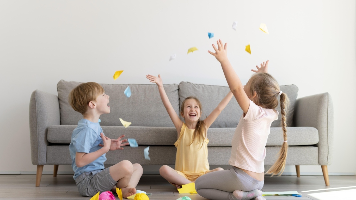 Дети играют на полу  в комнате с серым диваном