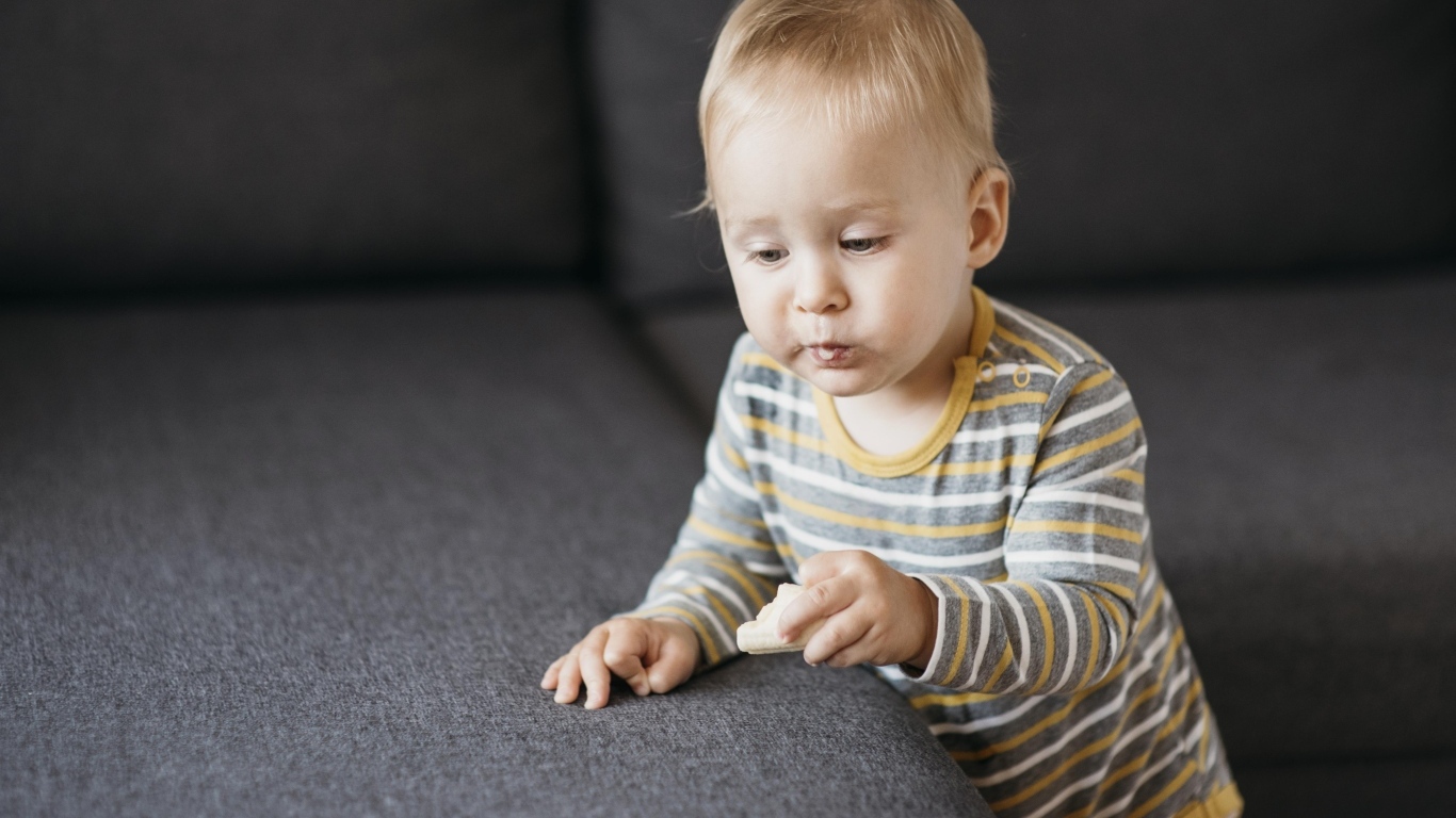 Любопытный маленький ребенок у дивана