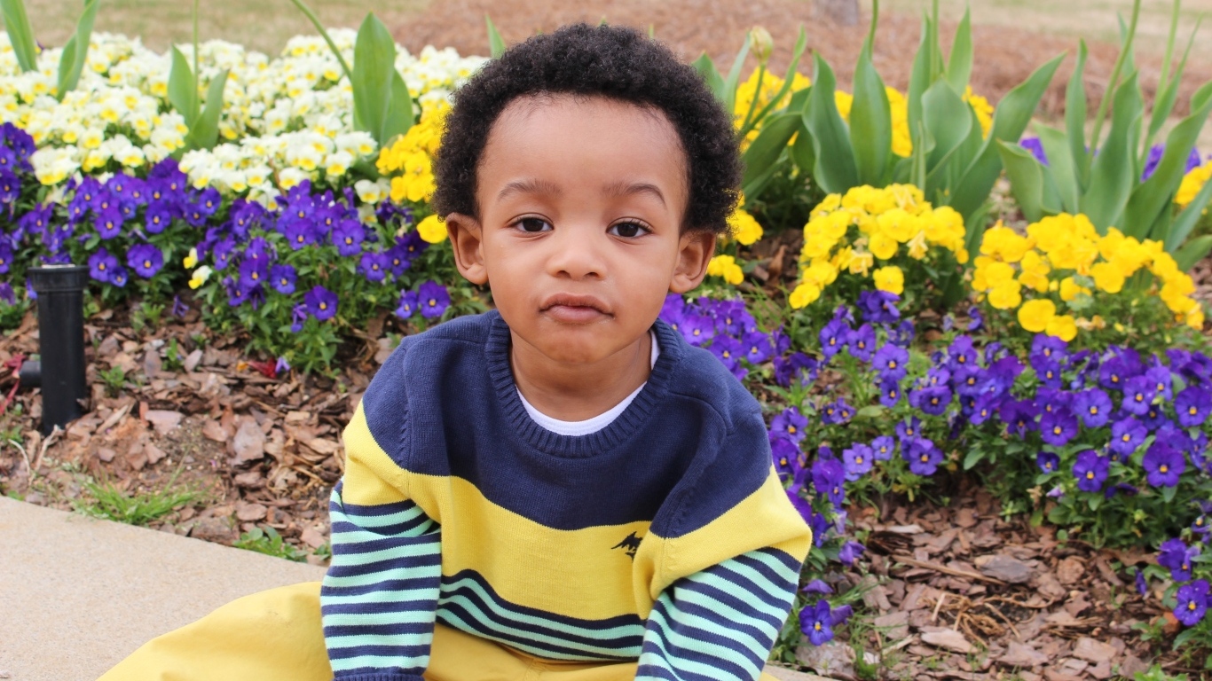 Темнокожий мальчик у клумбы с цветами 