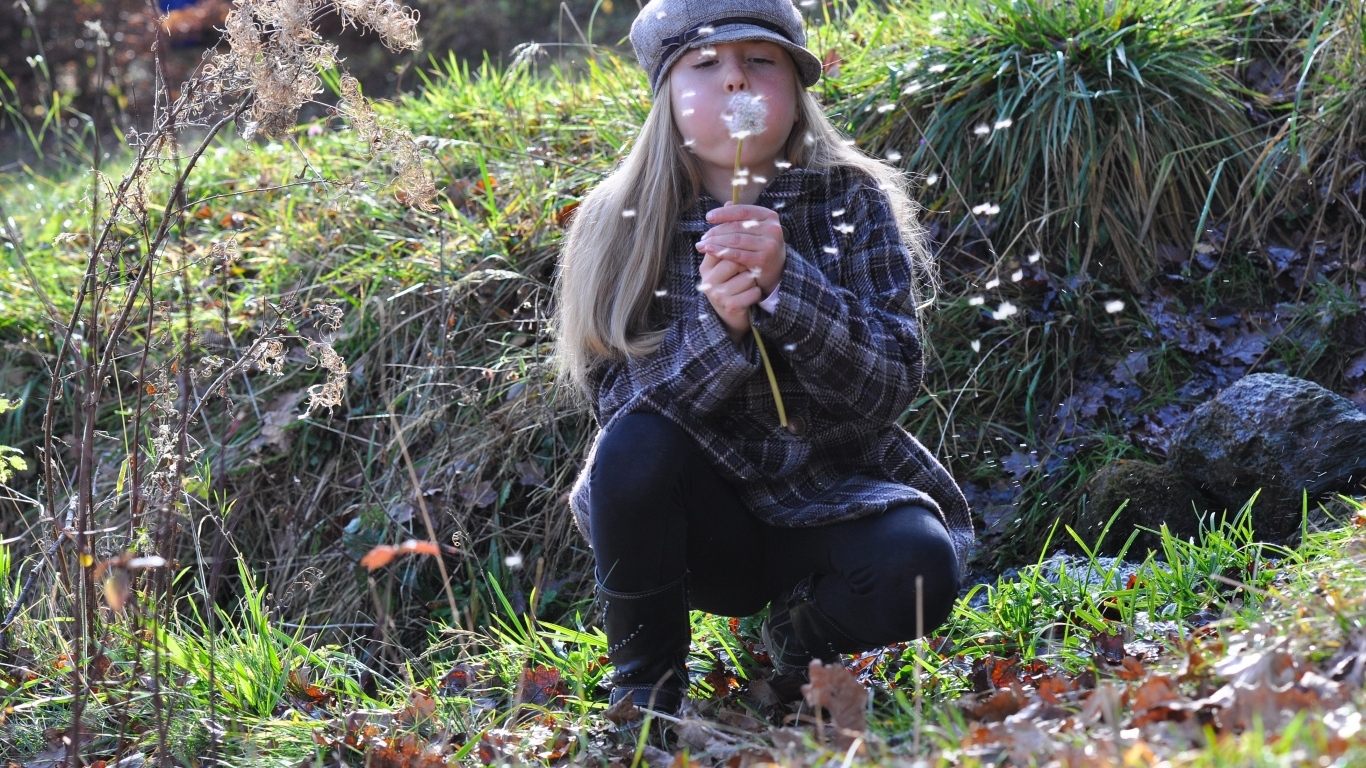 Девочка в кепке дует на одуванчик