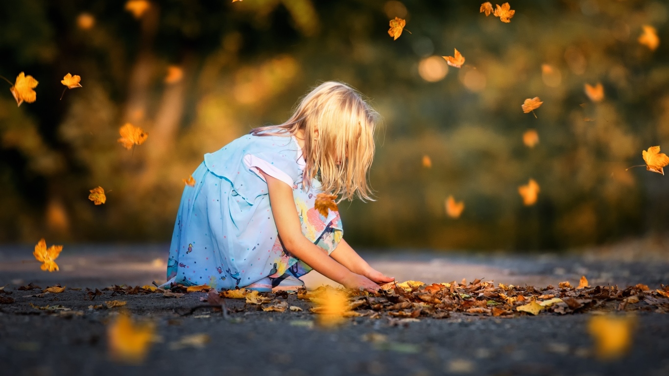 Девочка в платье играет с листьями на дороге