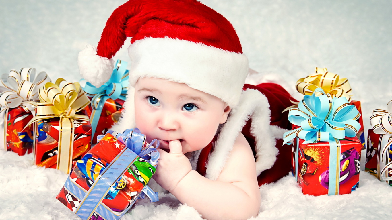Грудной ребенок в новогодней шапке с подарками на покрывале