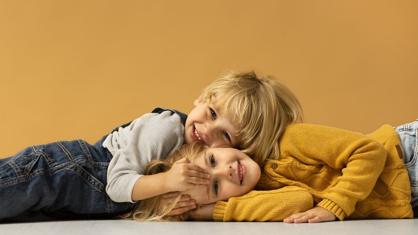 Маленькие брат и сестра лежат на полу на желтом фоне