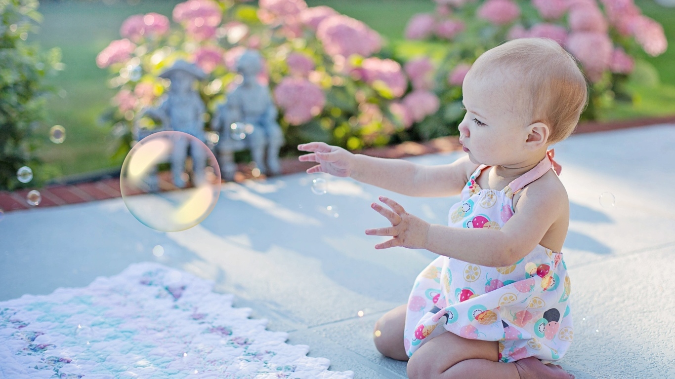 Маленькая девочка ловит мыльный пузырь