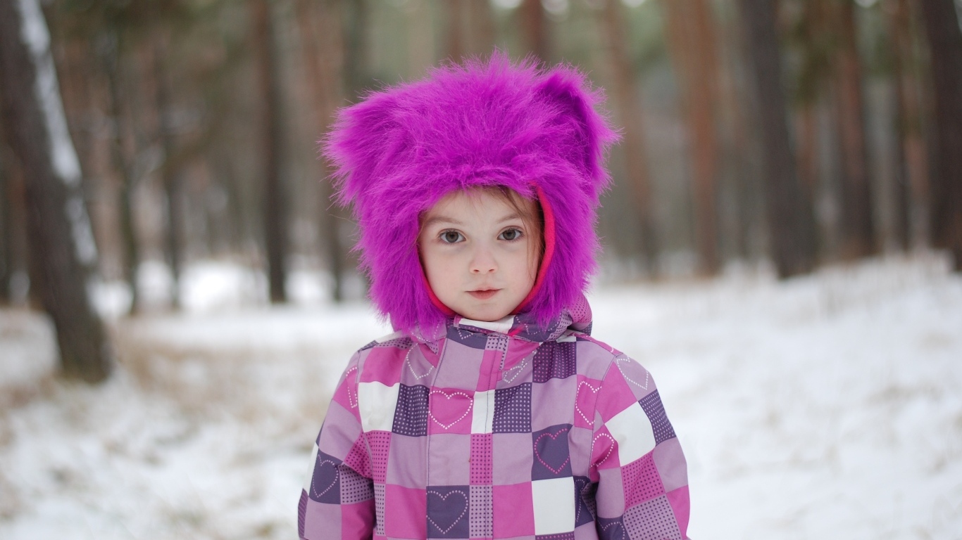 Маленькая девочка в меховой шапке в лесу зимой