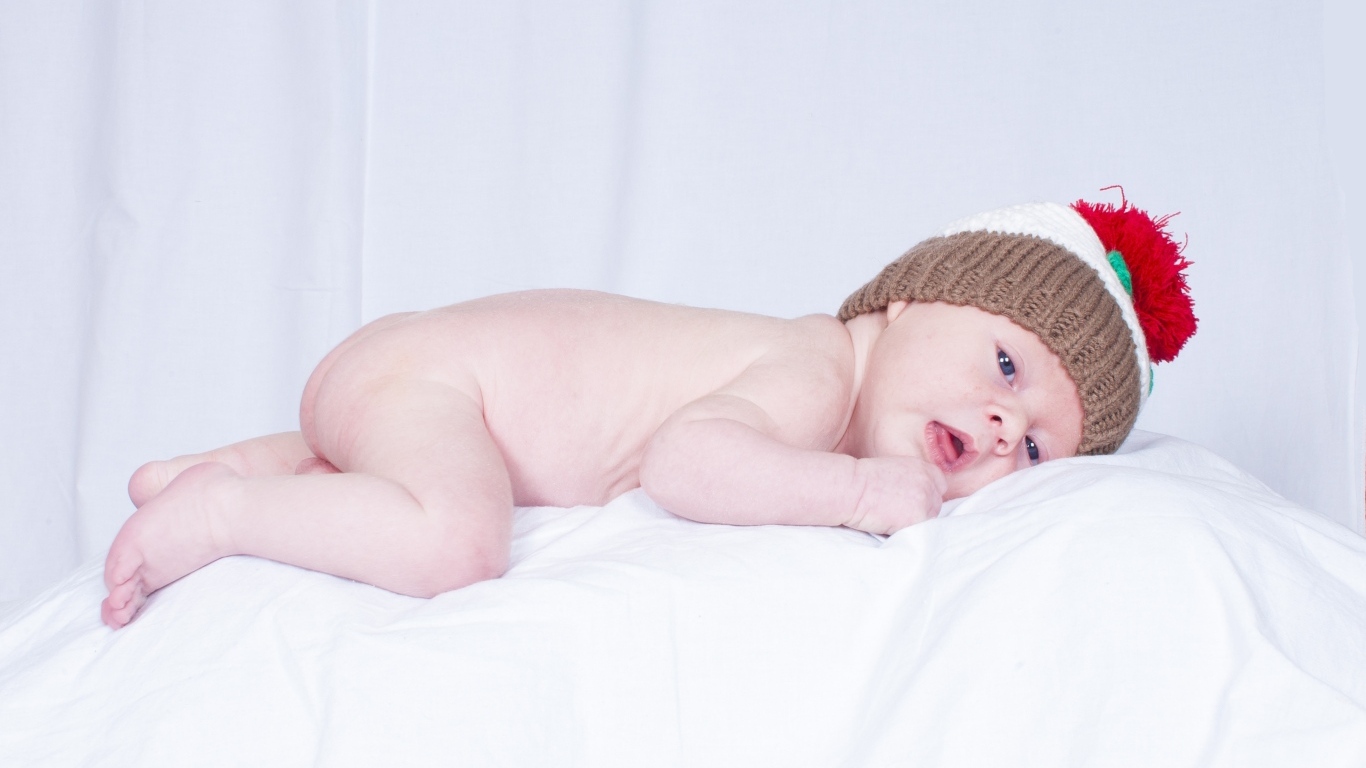 Новорожденный малыш в шапке на белой подушке