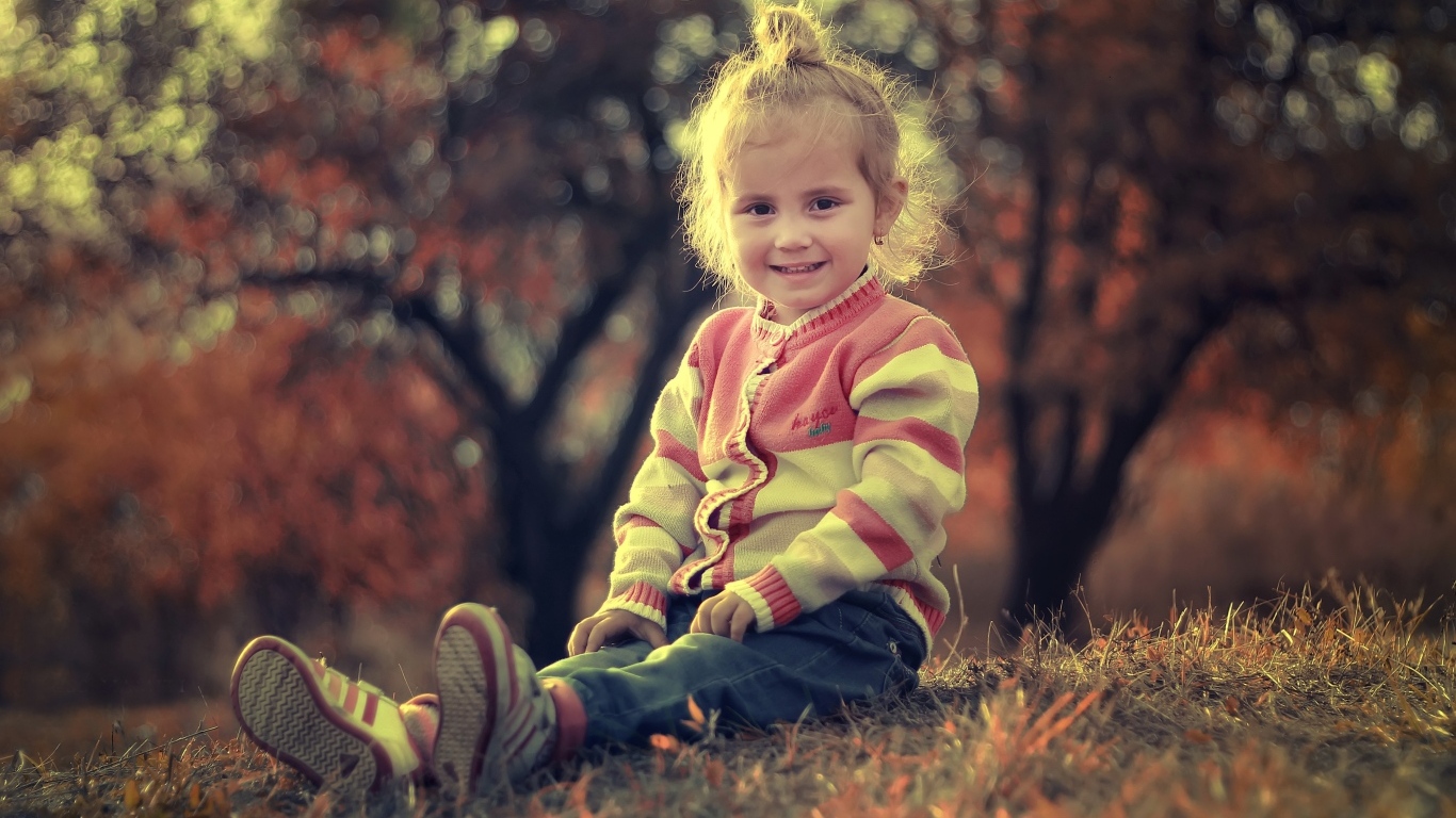 Настоящая маленькая девочка сидит на земле в лучах солнца