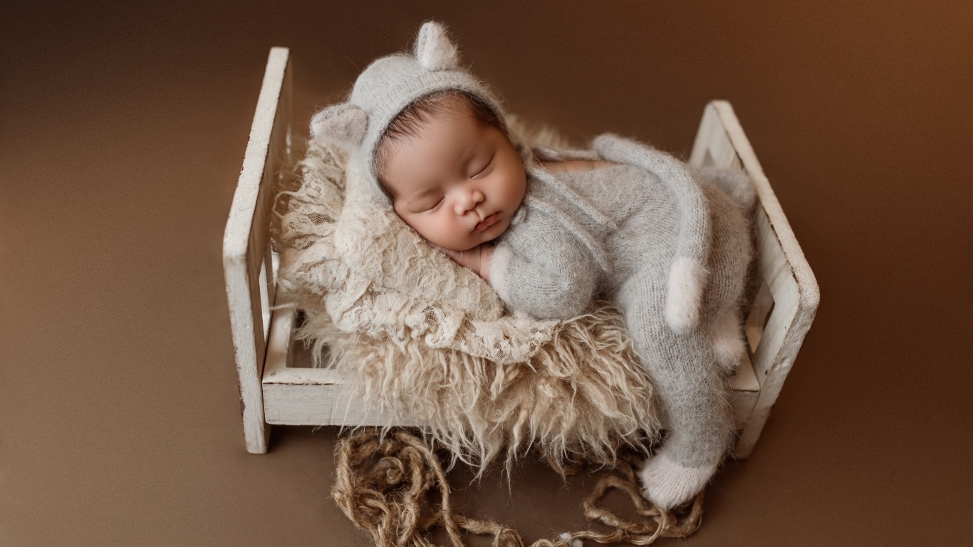 Спящий ребенок на маленькой кровати на коричневом фоне