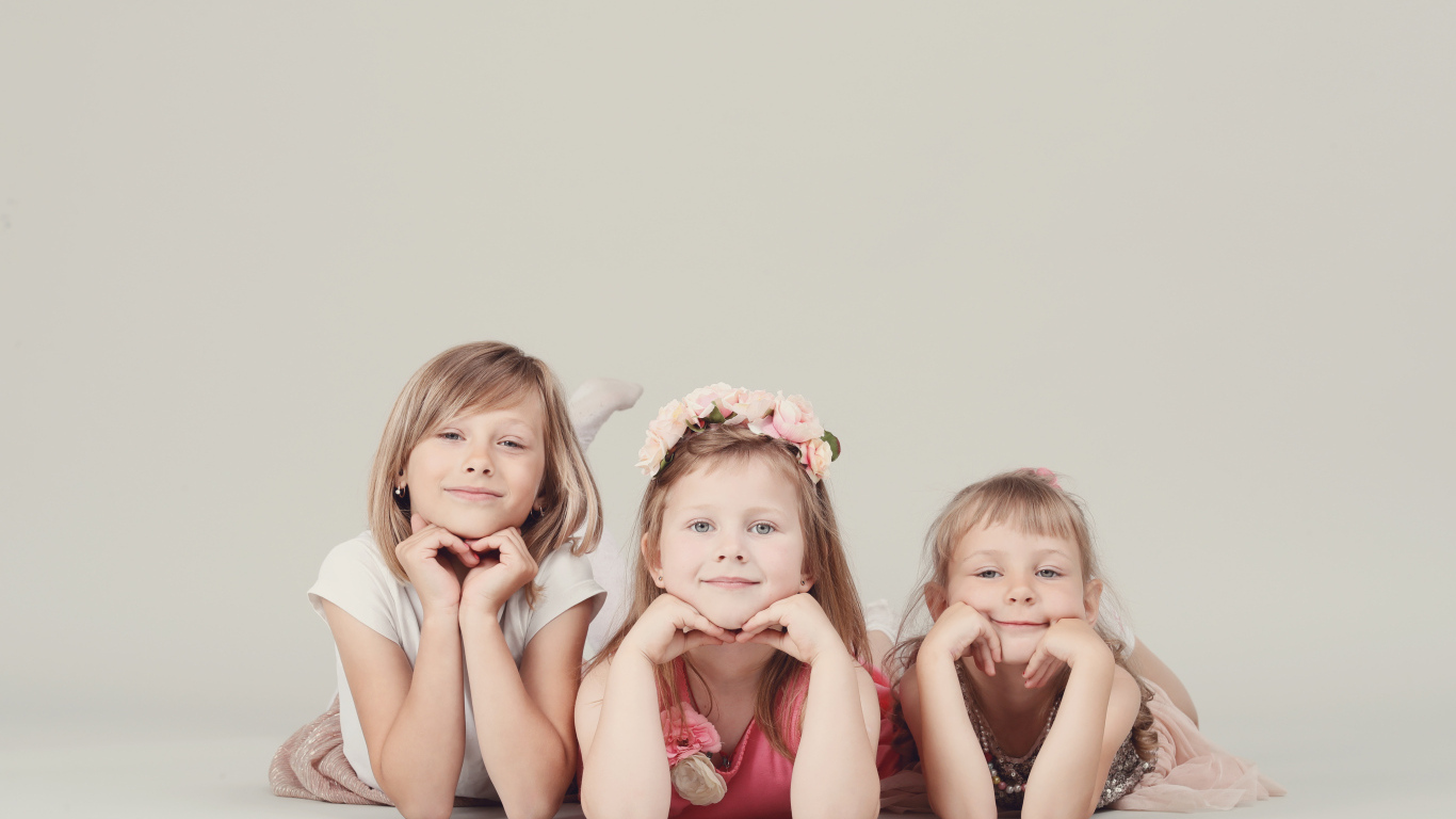 Три маленькие девочки лежат на сером фоне