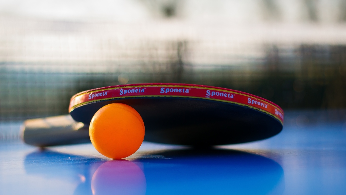 Ракетка и оранжевый мяч для пинг понга на столе