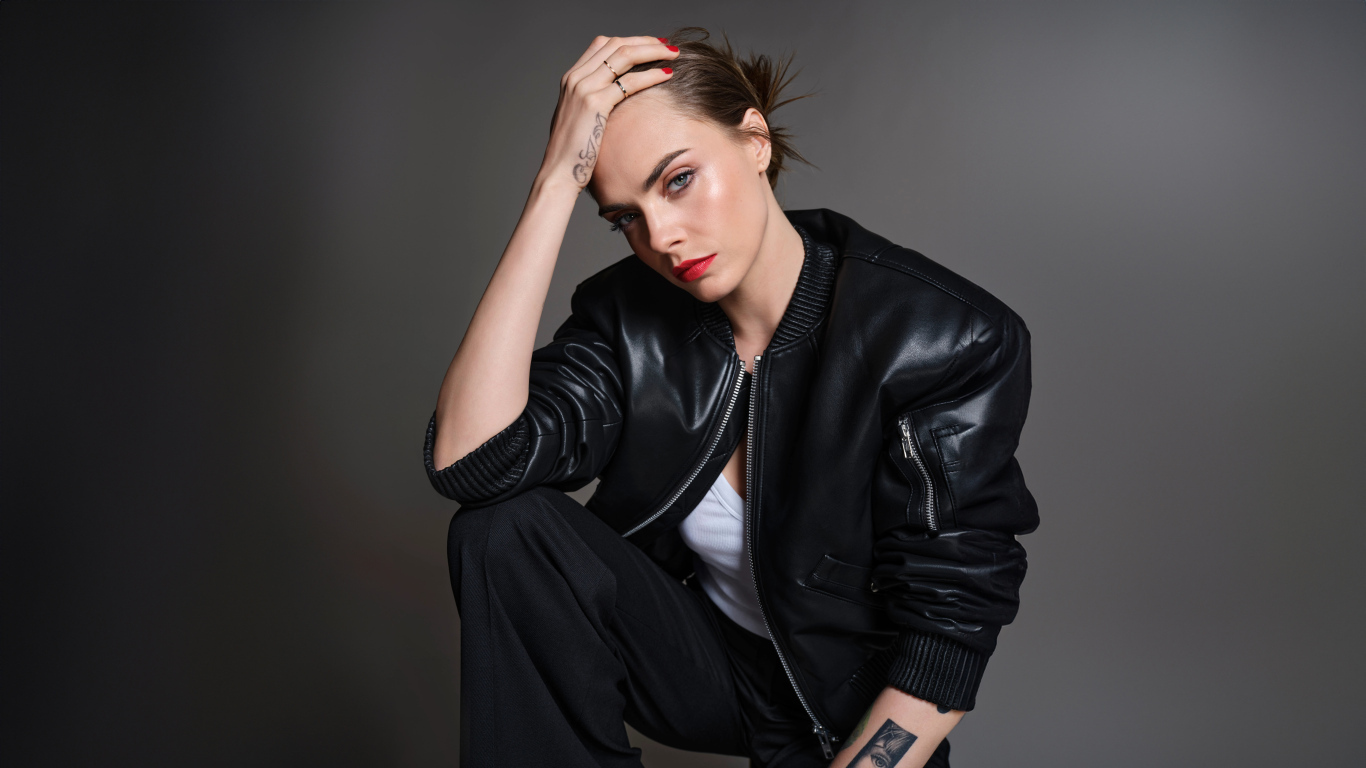 Актриса Кара Делевинь в черной кожаной куртке на сером фоне