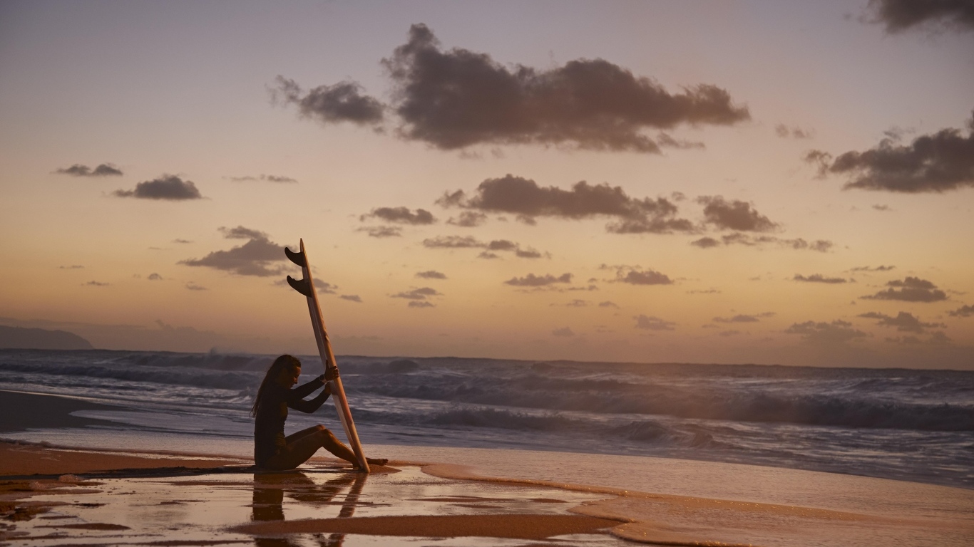 Девушка серфингистка сидит на берегу моря