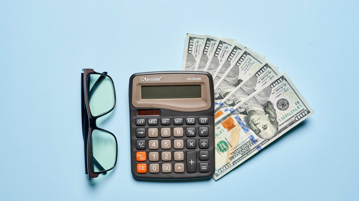 Очки, калькулятор и доллары на сером фоне