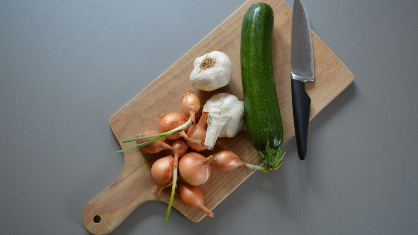 Лук, чеснок и кабачок на разделочной доске с ножом
