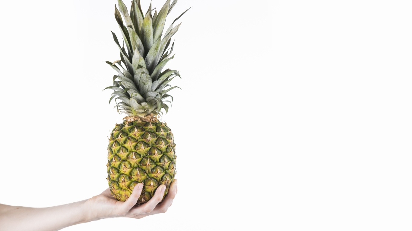 Большой ананас в руке на белом фоне
