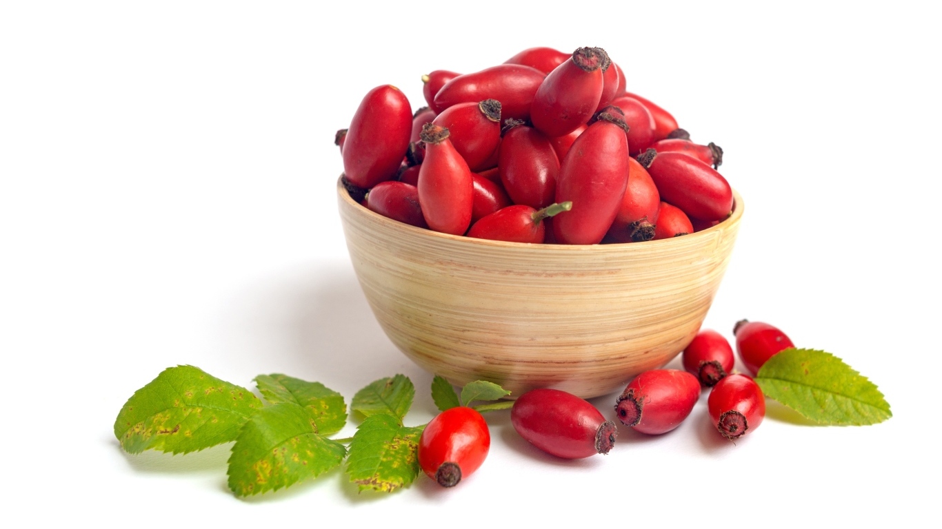 Тарелка с красными плодами шиповника на белом фоне